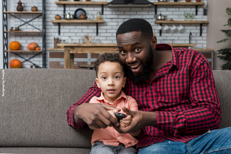 Pai e filho sentados no sofá com um controle de TV nas mãos