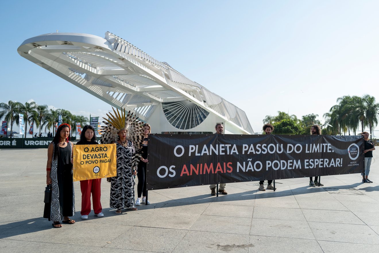 Voluntários, apoiadores e a influenciadora indígena Daiara Tukano posam para foto com banners em frente ao Museu do Amanhã