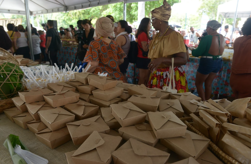 muitas marmitas em uma mesa com pessoas ao fundo