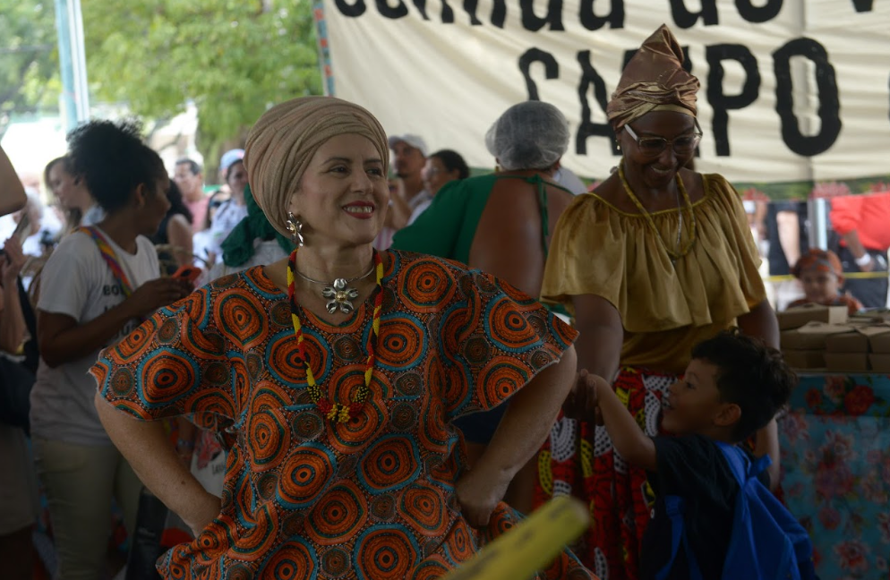 mulher branca com turbante e roupas coloridas com pessoas ao fundo
