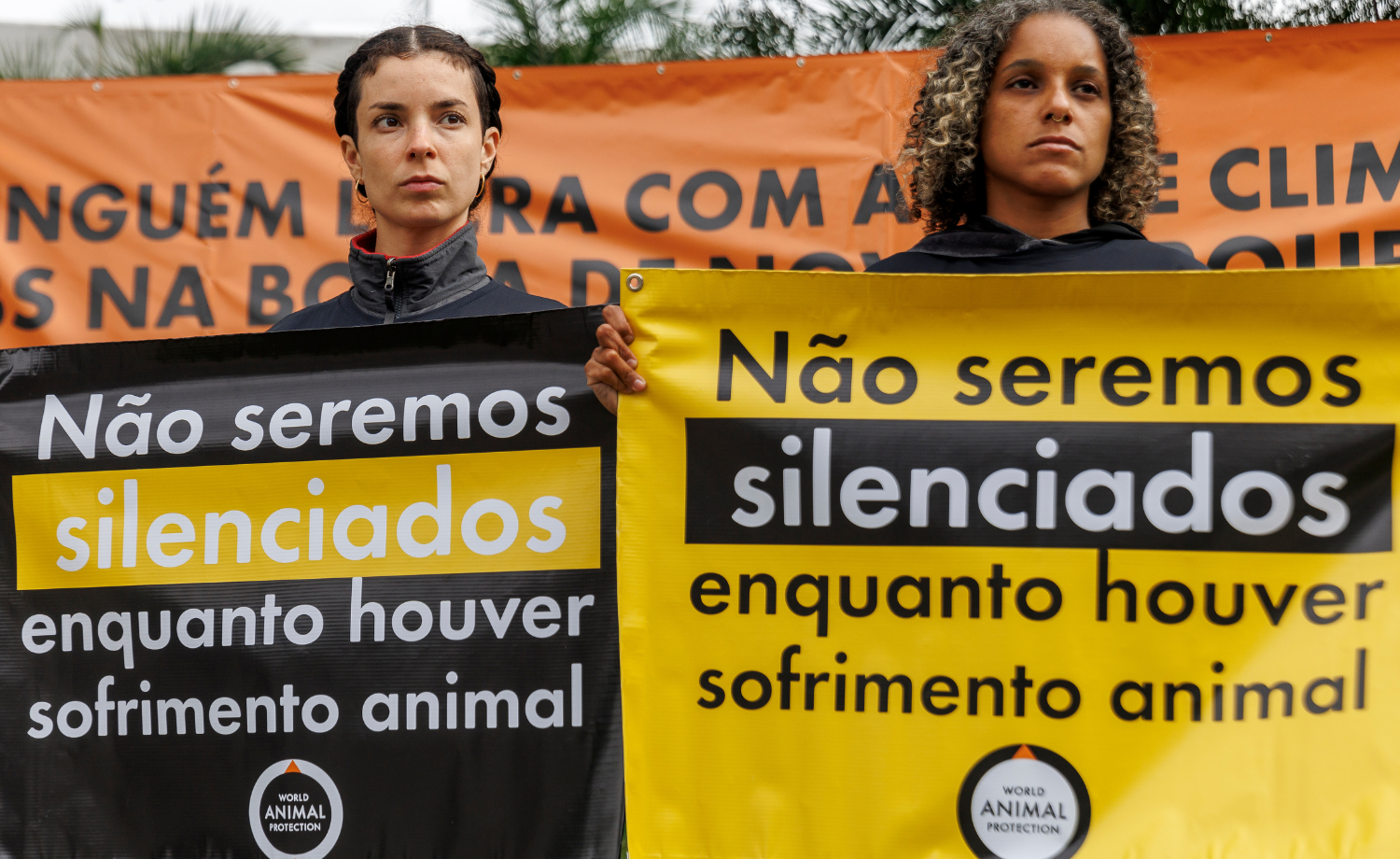 Duas ativistas seguram banners em ação contra a JBS. Os banners dizem: não seremos silenciados enquanto houver crueldade animal.