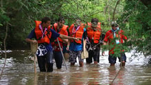 Grupo de cinco homens do movimento Escoteiros do Brasil, com coletes salva-vidas, andando em um rio que bate em seus joelhos.