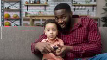 Pai e filho sentados no sofá com um controle de TV nas mãos