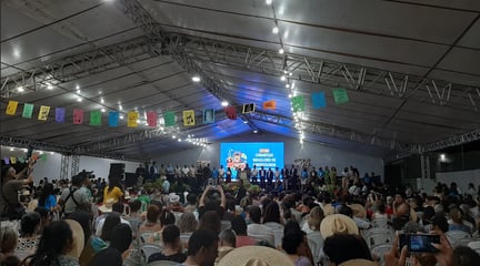 UM GALPÃO COM UMA PLATÉIA E BANDEIRINHAS E UM TELÃO NO FUNDO