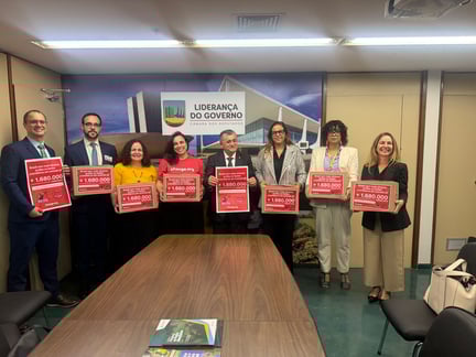 Membros da Câmara e da Agenda Animal Legislativa posam para foto em celebração à aprovação do PL 3062 de 2022. Na imagem, 8 pessoas (3 homens e 5 mulheres) estão em pé, atrás de uma mesa, e seguram cartazes com os dizeres "Brasil sem mais atrasos: proíba os testes cosméticos em animais já! Mais de 1.680.000 assinaturas)".