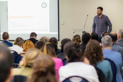 Daniel Cruz, coordenador de bem-estar animal, está em um palanque, ao lado de uma projeção, durante palestra no Simpósio do Produtor do Bem.