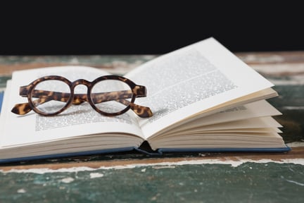 Livro aberto com um óculos de grau redondo em cima das páginas