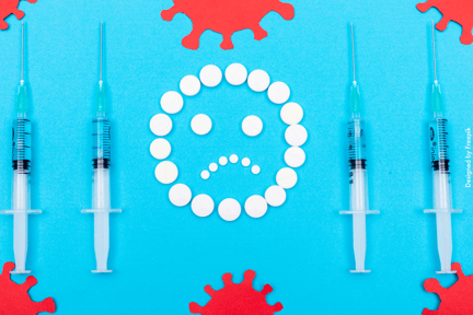 Fundo azul com imagens de bactérias nas pontas. No centro, uma carinha triste feita com remédios. Nas duas pontas, duas seringas.