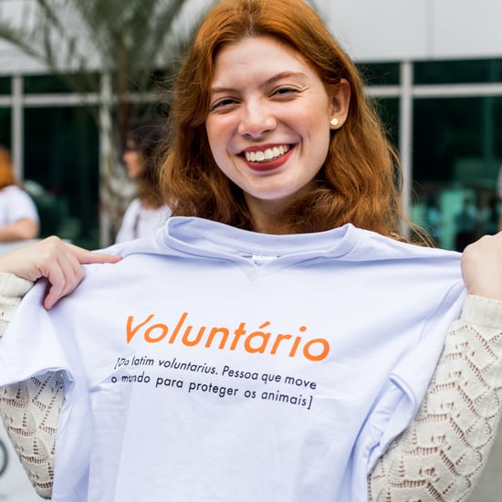 Imagem de uma mulher ruiva sorrindo segurando uma camiseta escrito voluntário.