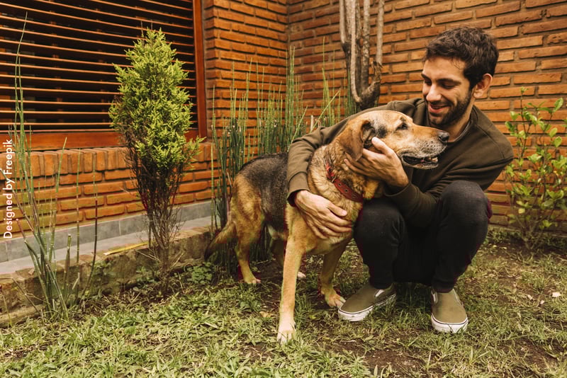 Tutor com seu cão no jardim, abaixando, abrançando-o